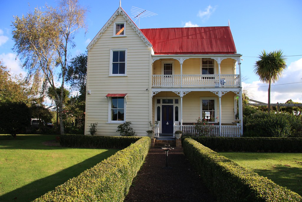 Classic two-storey New Zealand villa with a red roof behind a trimmed hedge